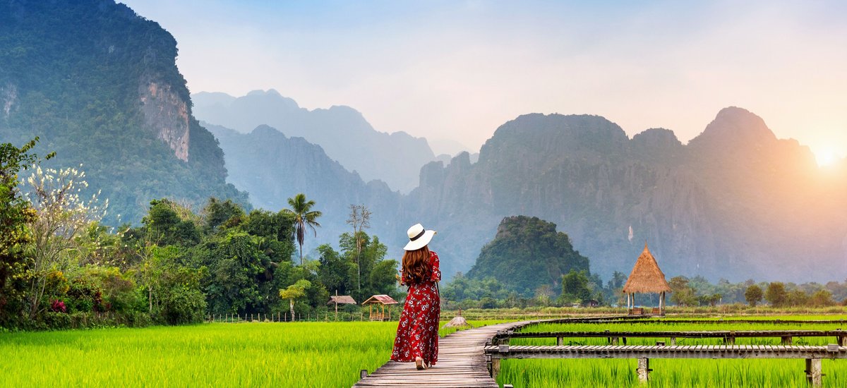Jeune femme marchant sur un chemin en bois avec un champ de riz vert à Vang Vieng, Laos.