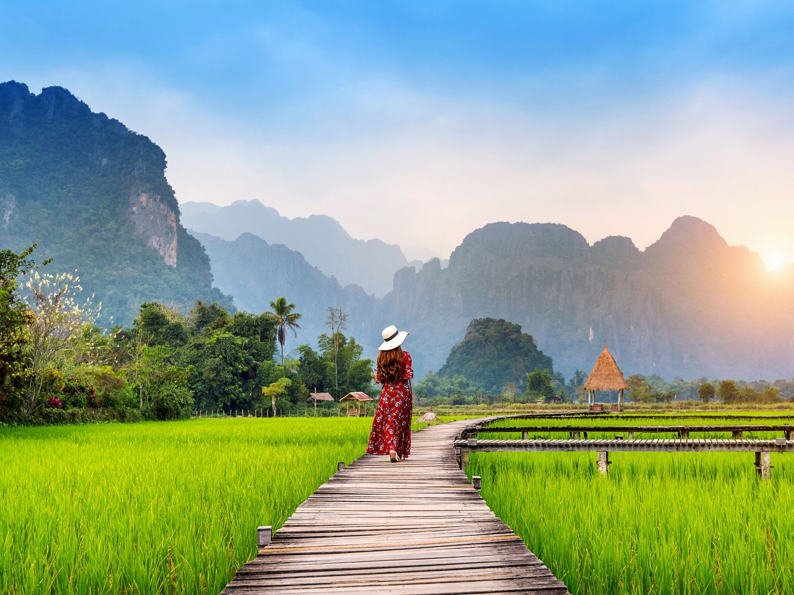 Jeune femme marchant sur un chemin en bois avec un champ de riz vert à Vang Vieng, Laos.