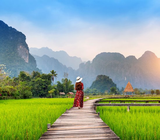 Jeune femme marchant sur un chemin en bois avec un champ de riz vert à Vang Vieng, Laos.