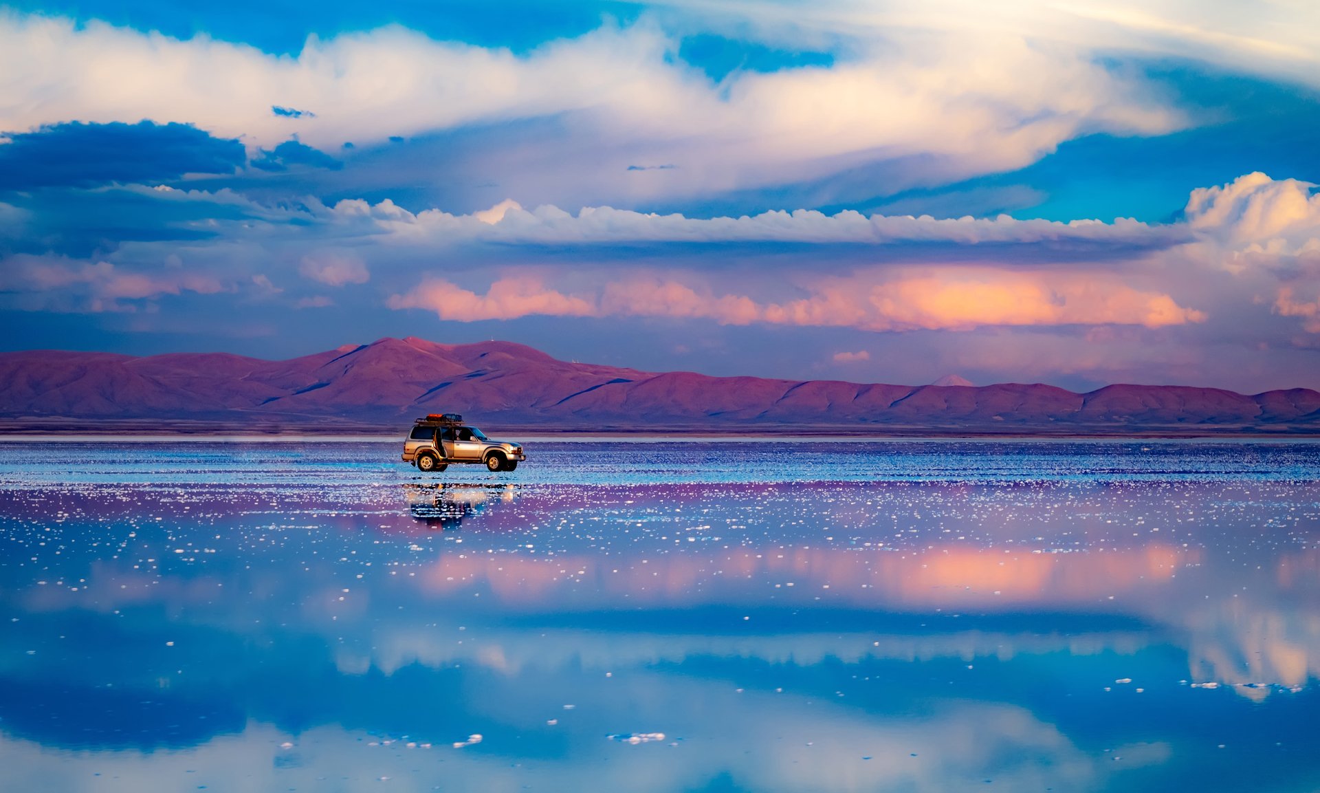 Voiture debout au milieu d'un plat de sel reflétant le ciel bleu, Salar de Uyuni, Bolivie