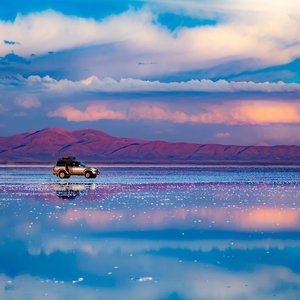 Voiture debout au milieu d'un plat de sel reflétant le ciel bleu, Salar de Uyuni, Bolivie