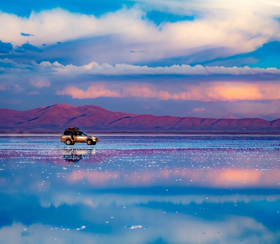 Voiture debout au milieu d'un plat de sel reflétant le ciel bleu, Salar de Uyuni, Bolivie